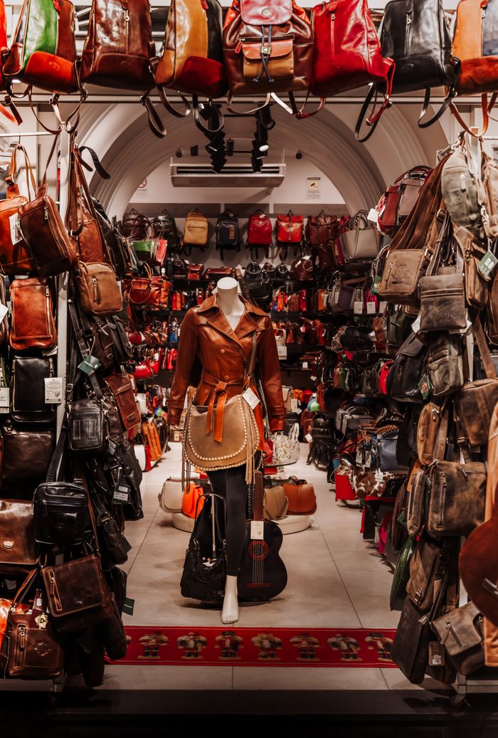 services-01 A vibrant indoor leather goods store with a mannequin dressed in leather clothing, surrounded by various bags.