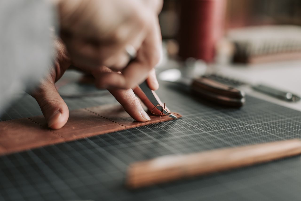 our-experience Close-up of hands intricately working on a leather piece in a crafting workshop.