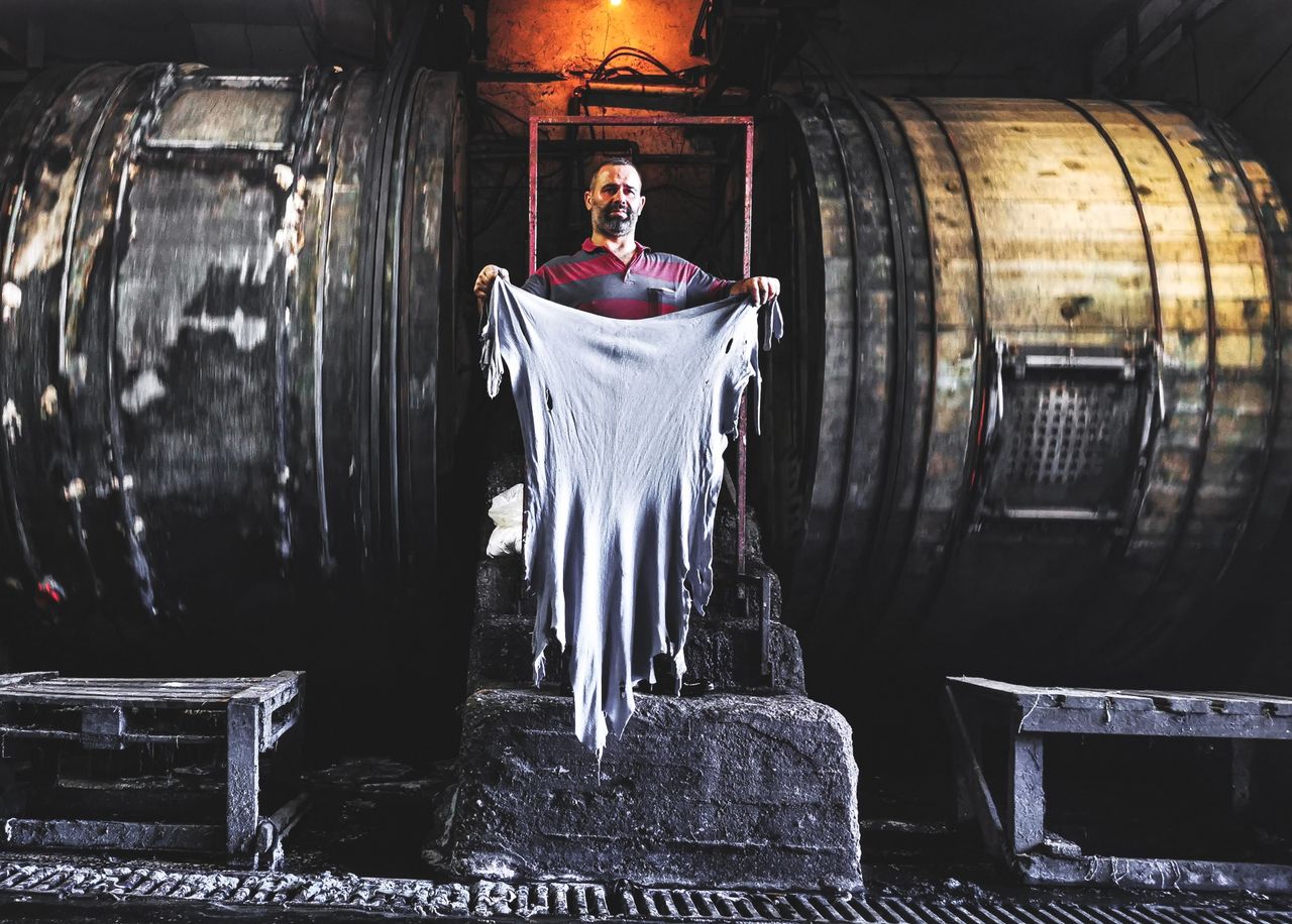 services-04 Mature bearded male showing textile between wooden barrels while standing on stone stairs and looking at camera