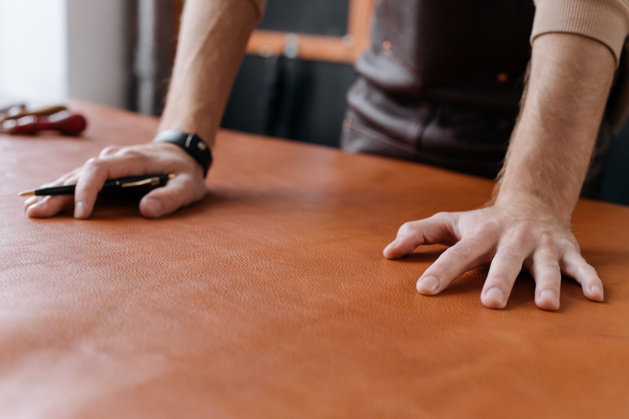 about-img Detailed shot of a leatherworker’s hands working with brown leather, highlighting craftsmanship and precision.